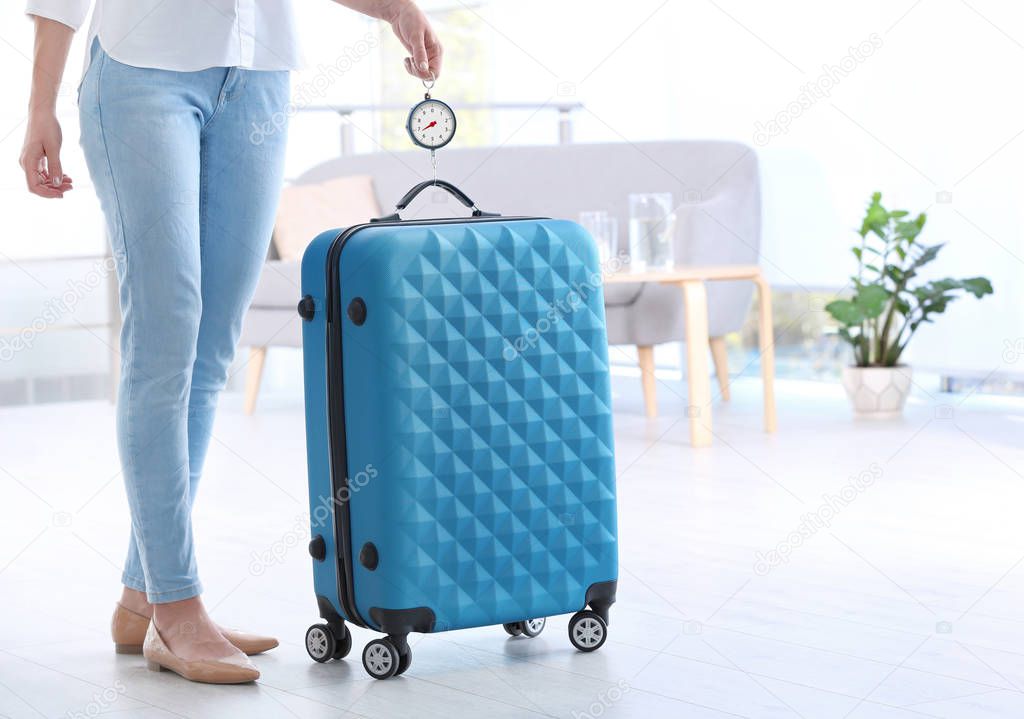 Woman weighing suitcase indoors. Space for text
