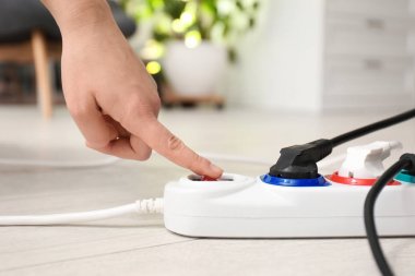 Kadın, evin içinde yerde, uzatma kablosunun düğmesine basıyor, yakın plan. Elektrikçinin profesyonel ekipmanı