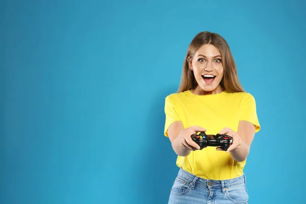 Mujer joven emocional jugando videojuegos con controlador en el fondo de color. Espacio para texto —  Fotos de Stock