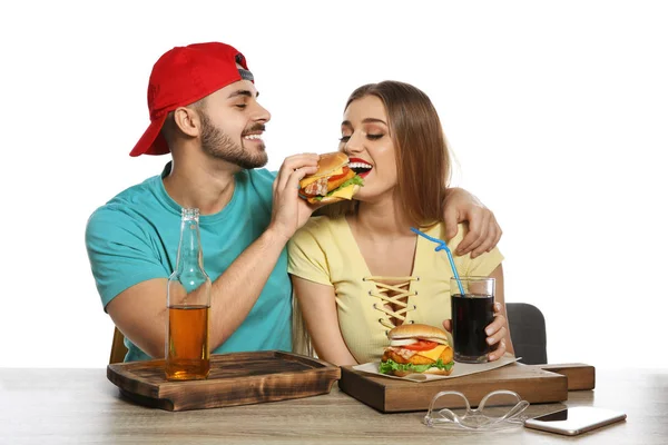 Glückliches Paar beim Mittagessen mit Burgern am Tisch auf weißem Hintergrund — Stockfoto