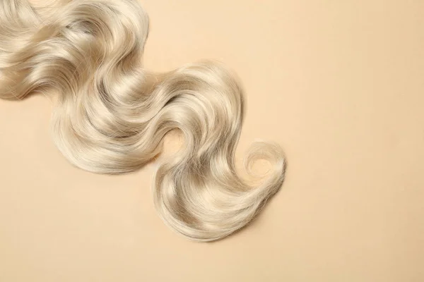 Bloqueio de cabelo ondulado loiro no fundo da cor, vista superior. Espaço para texto — Fotografia de Stock