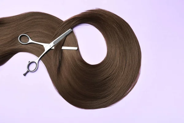 Lock of brown straight hair and thinning scissors on color background, flat lay — Stock Photo, Image
