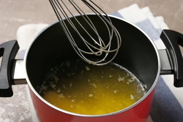 Pot with melting butter and whisk on table, closeup — Stock Photo, Image