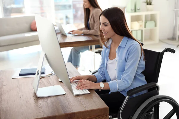 Jonge vrouw in rolstoel met behulp van computer op het werk — Stockfoto