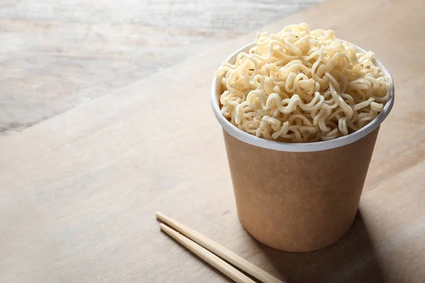 Tazza di carta di tagliatelle istantanee e bacchette sul tavolo. Spazio per testo — Foto Stock