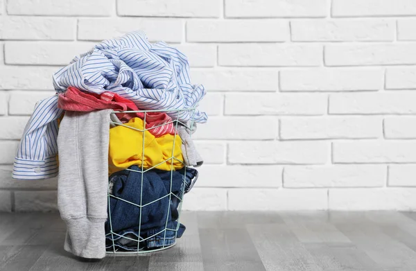 Laundry basket with dirty clothes on floor near brick wall. Space for text — Stock Photo, Image