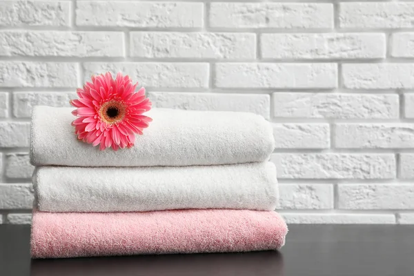 Stack of folded soft towels with flower on table near brick wall. Space for text — Stock Photo, Image