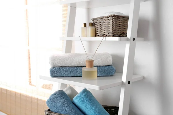 Shelving unit with clean towels and toiletries near white wall — Stock Photo, Image