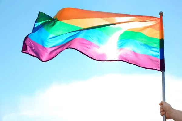 Gay hombre la celebración de arco iris LGBT bandera contra azul cielo — Foto de Stock