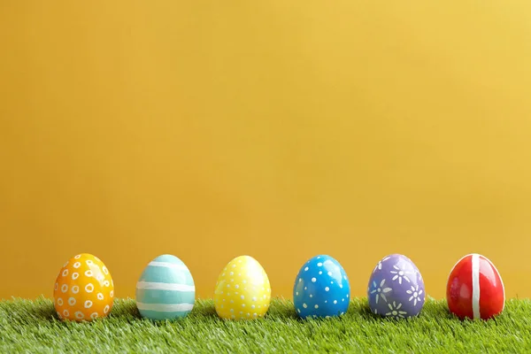 Malovaná velikonoční vajíčka na zelené trávě proti barevnému pozadí, prostor pro text — Stock fotografie