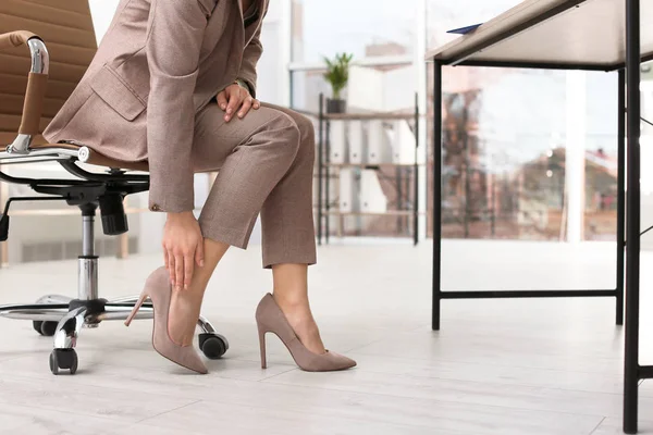 Young woman suffering from leg pain in office, closeup with space for text — Stock Photo, Image