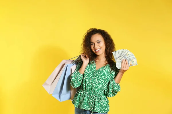 Ung afro-amerikansk kvinna med pengar och shoppingväskor på färg bakgrund — Stockfoto