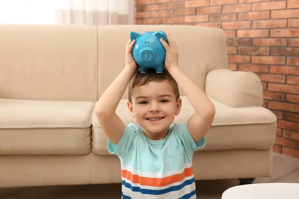 Little boy with piggy bank at home. Saving money