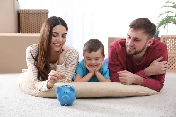 Lycklig familj med sparbössor och pengar på golvet hemma — Stockfoto