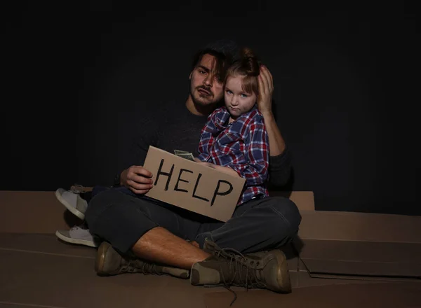 Pobre pai e filha com sinal AJUDA no chão perto da parede escura — Fotografia de Stock