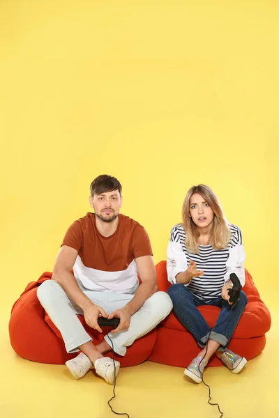 Emotional couple playing video games with controllers on color background. Space for text