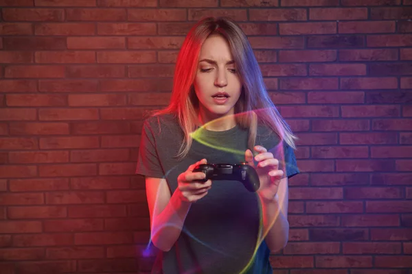 Emocional joven mujer jugando videojuegos con controlador cerca de la pared de ladrillo —  Fotos de Stock