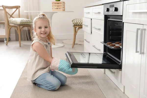 Маленькая девочка открывает дверь духовки с печеньем на кухне — стоковое фото