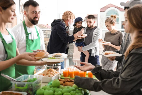 Volunteers giving food to poor people indoors