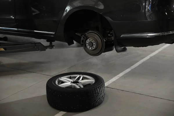 Rueda en el piso cerca de coche levantado en el taller de reparación de automóviles —  Fotos de Stock