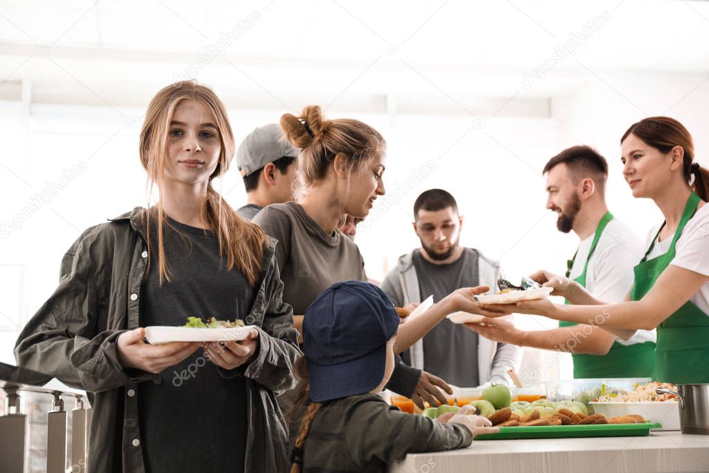 Teenage girl with other poor people receiving food from volunteers indoors
