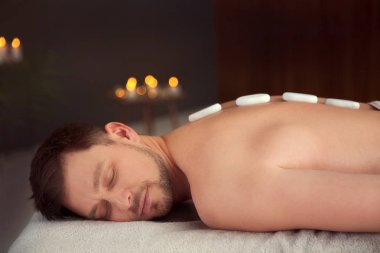 Yakışıklı adam spa salonunda sıcak taş masajı alan