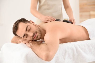 Yakışıklı adam spa salonunda sıcak taş masajı alan
