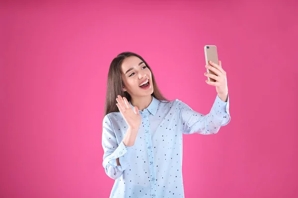 Mulher usando telefone celular para bate-papo de vídeo em fundo de cor — Fotografia de Stock