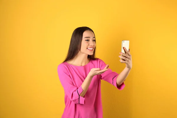 Femme utilisant un téléphone mobile pour le chat vidéo sur fond couleur — Photo