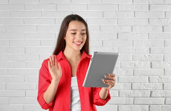 Mujer utilizando la tableta para el chat de vídeo contra la pared de ladrillo. Espacio para texto — Foto de Stock