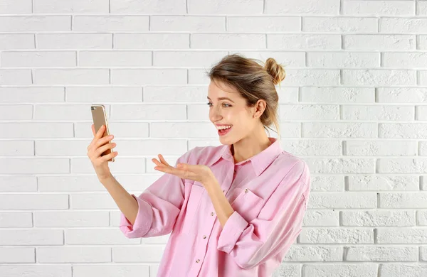 Mulher usando telefone celular para bate-papo de vídeo contra parede de tijolo — Fotografia de Stock