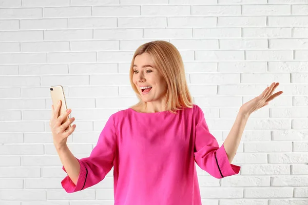 Mulher usando telefone celular para bate-papo de vídeo contra parede de tijolo — Fotografia de Stock