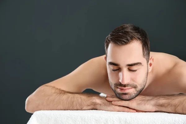 Homem bonito relaxando na mesa de massagem contra fundo preto, espaço para texto. Serviço de Spa — Fotografia de Stock