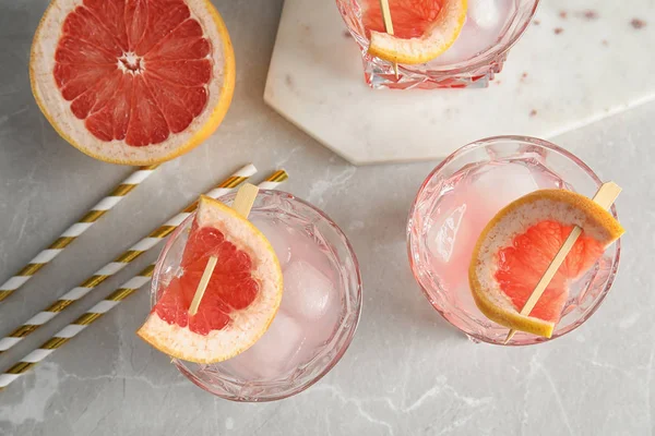 Плоская композиция с бокалами грейпфрутовых коктейлей на сером столе — стоковое фото