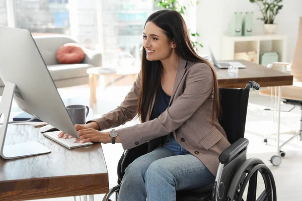 Mujer joven en silla de ruedas usando computadora en el lugar de trabajo — Foto de Stock