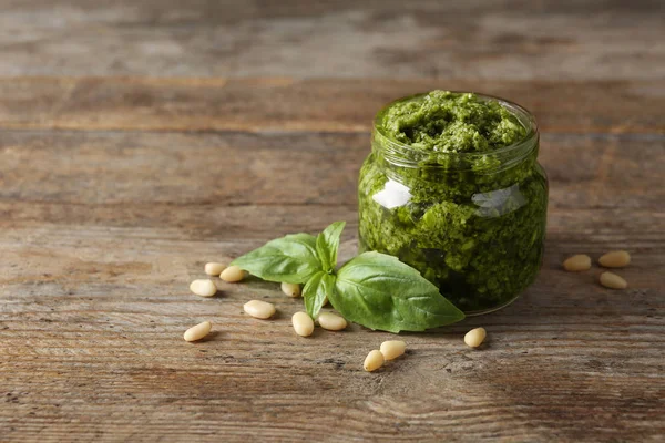 Jar of pesto sauce with basil leaves and pine nuts on wooden table. Space for text