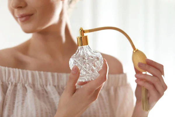 Young woman with bottle of perfume on blurred background, closeup — Stock Photo, Image