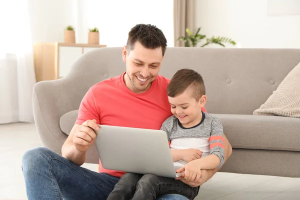 Хлопчик і його батько з ноутбуком сидить біля дивана на підлозі. Сімейного часу — стокове фото