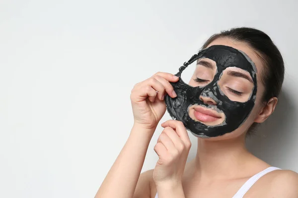 Beautiful young woman removing black mask from her face on white background. Space for text — Stock Photo, Image