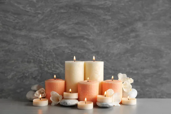 Όμορφη σύνθεση με κεριά, λουλούδια και πέτρες στο τραπέζι σε γκρίζο φόντο. Χώρος για κείμενο — Φωτογραφία Αρχείου