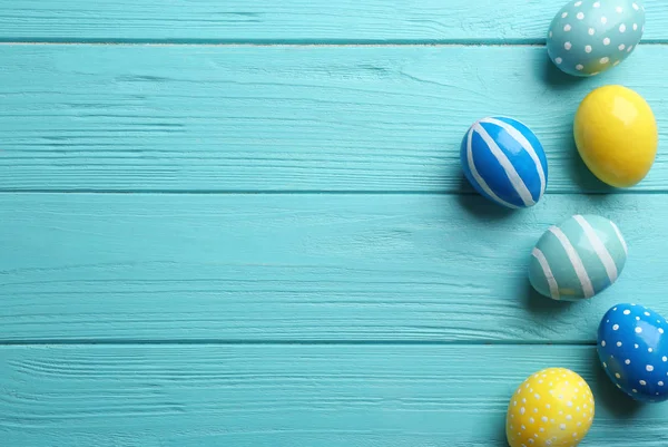 Flat lay composition of painted Easter eggs on wooden table, space for text