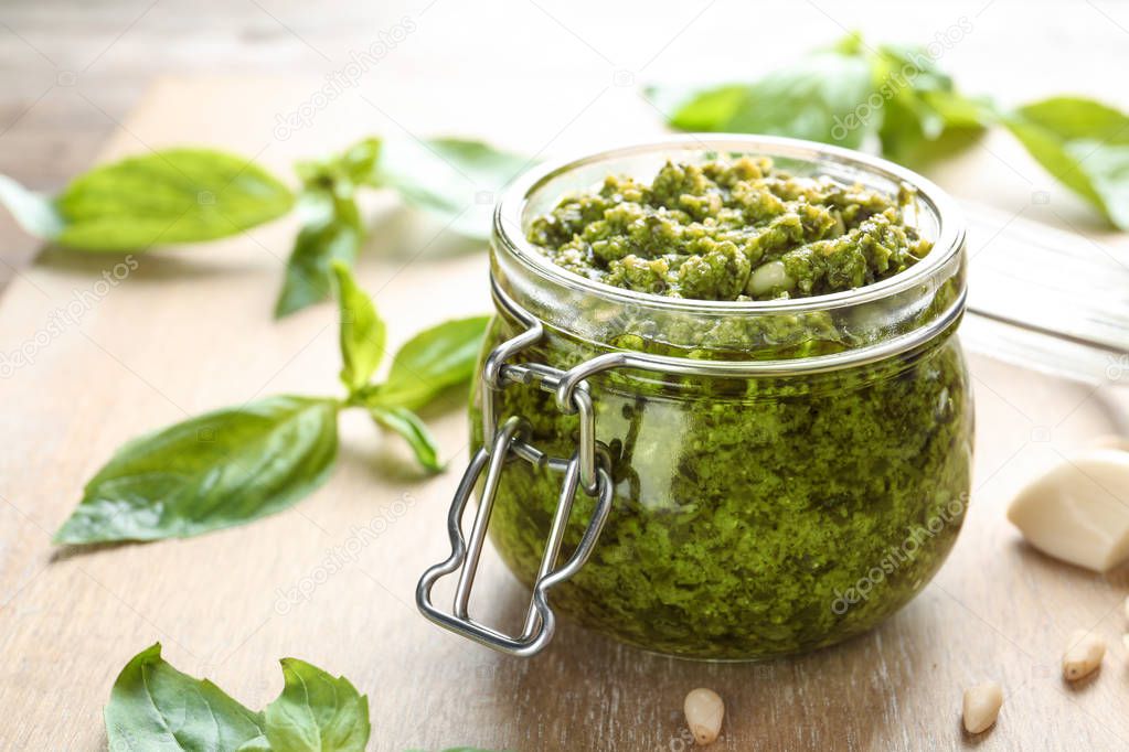 Jar of tasty pesto sauce on table, closeup. Space for text