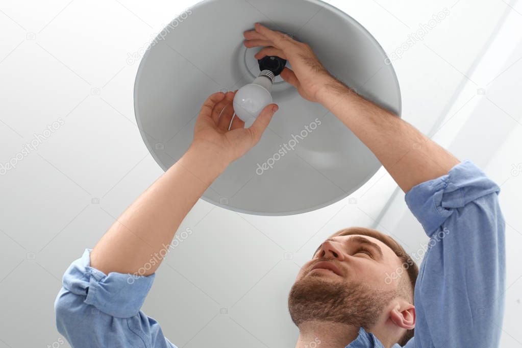 Man changing light bulb in lamp indoors