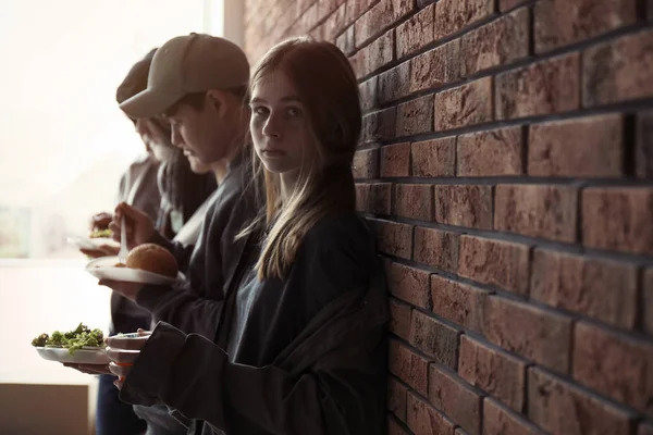 Adolescente e outras pessoas pobres com comida na parede de tijolos dentro de casa. Espaço para texto — Fotografia de Stock