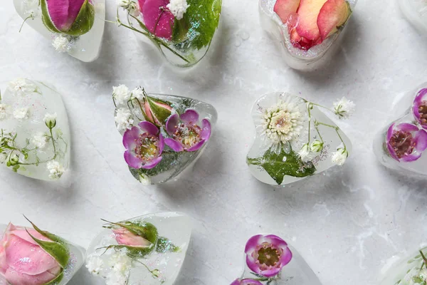 Cubes de glace en forme de coeur avec des fleurs sur fond gris, plat — Photo