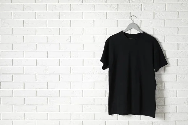 Hanger with black t-shirt against brick wall. Mockup for design — Stock Photo, Image