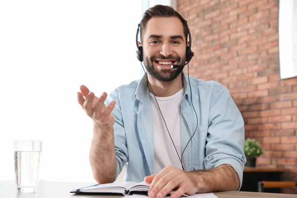 Young man with headset looking at camera and using video chat in home office — 스톡 사진