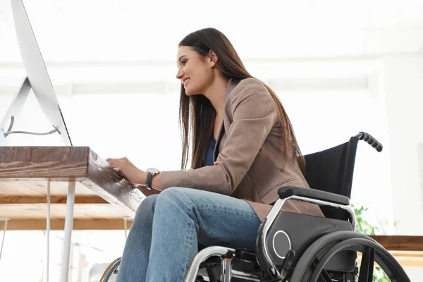 Jonge vrouw in rolstoel met behulp van computer op het werk — Stockfoto