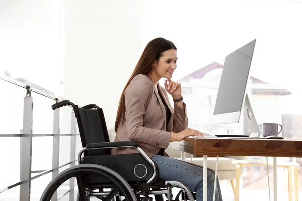 Jonge vrouw in rolstoel met behulp van computer op het werk — Stockfoto