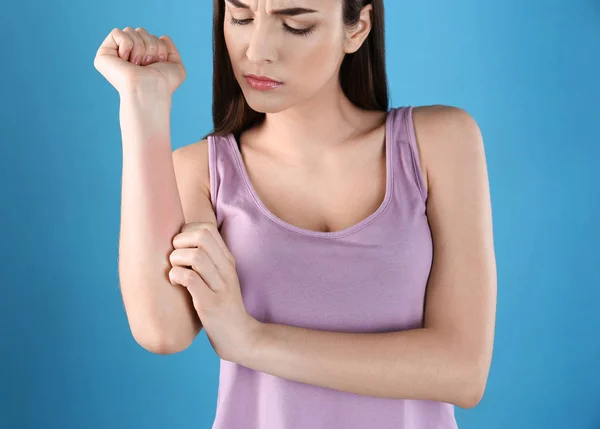 Молодая женщина царапала руку на цветном фоне. Симптомы аллергии — стоковое фото